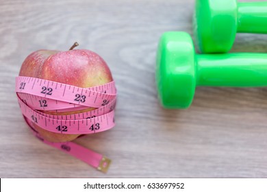 Red Apple Close Up With Green Dumb Bells And Measuring Tape. Diet And Work Out Concept Related