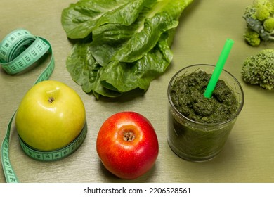 Red apple, measuring tape around green apple. Green smoothie in glass. Broccoli and lettuce on table. Top view. Green background. - Powered by Shutterstock