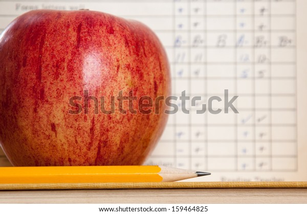 Red apple on a book with pencil and vintage\
report card in background