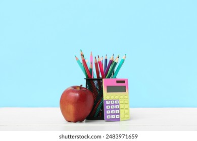 Red apple with pencils in holder and calculator on table against blue background - Powered by Shutterstock