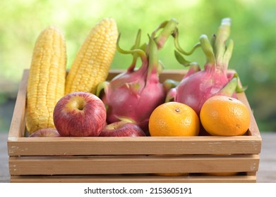 Red Apple, Yuzu Orange, Corn, Dragon Fruit, Packed In A Wooden Box With Blurred Green Background. (Choose Focus On Apples And Oranges). Red Contain Lycopene. Yellow Contain Carotenoids, Vitamin C.