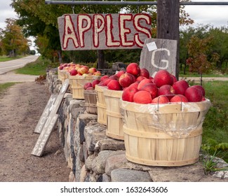 Red apples in a basket with a hand painted apple sign. Gala, Honey crisp, Macintosh apples. sitting on a stone wall in Northern Michigan. Road side stand. Organic. Healthy option food.