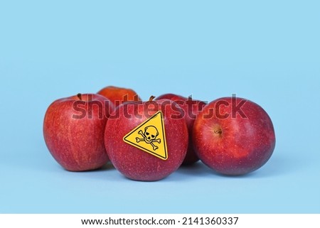 Red apples with poison skull symbol sticker on blue background. Concept of pesticide residues in agricultural food 