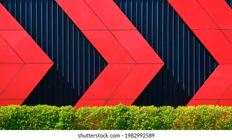 Red Arrow Pattern On Black Corrugated Metal Wall Behind Green Bush Fence, Exterior Architecture Decoration Design Concept