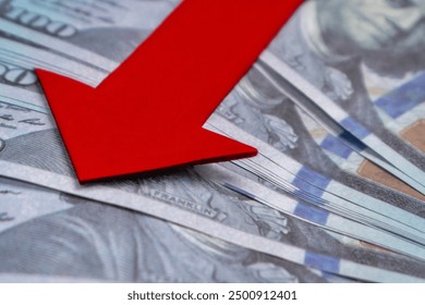 A red arrow pointing downwards on top of a pile of US dollar bills. Economic recession, financial decline, economic downturn concept.