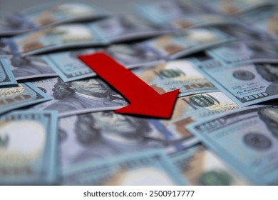 A red arrow pointing downwards on top of a pile of US dollar bills. Economic recession, financial decline, economic downturn concept.