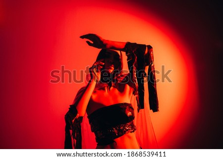 Red art portrait. Neon light. Surreal performance. Woman in trance wearing rags posing dramatic gesturing in orange magenta pink color gradient illumination on dark empty space background.