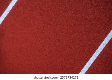 Red athletic track surface featuring white lane markings under a clear sky, inviting runners to start their training or a race in a sports facility.