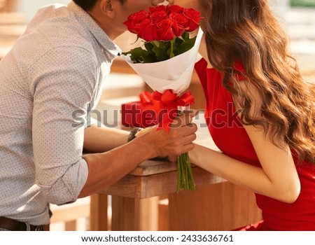 Red Attire of Elegant Woman Kissing Husband Behind Red Roses Bouquet