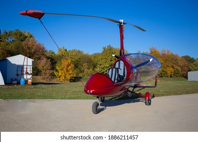 Red autogyro parked at the airfield in sunny day. Gyrocopter against the blue sky.
