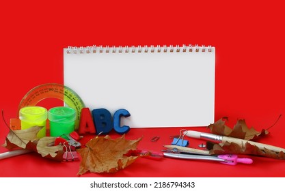 red background with school stationery, back to school concept, empty notebook, autumn theme