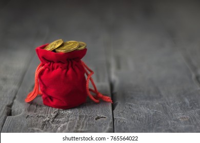 Red bag full of coins on a wooden table.