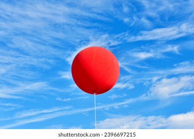 Red balloon. A giant inflatable red advertising balloon floats in the sunny blue sky. - Shutterstock ID 2396697215