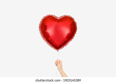 Red Balloon of heart shaped foil on white background in girl's hand. Valentine's Day or wedding party decoration.