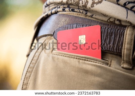 A red bank card lies in the pocket of light trousers. The man has a bank card in his pocket.