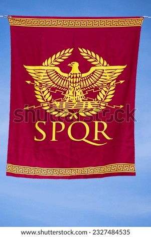 red banner in vertical view with a symbol from ancient roma, formed by an eagle and a laurel wreath and the legend SPQR. Senatus Populus que Romanus