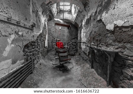 Red Barber chair in a run down prison cell in black and white