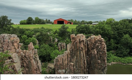 Red Barn In Field Above A Natural Stone Palisade And River On A Cloudy Day