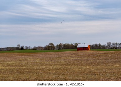 Red Barn in the Middle of Empty Field with Pink Sun Set Blue Sky on Spring Evening Day