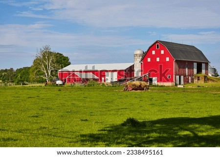Red barn on farmland with hay bales on feeder in summer