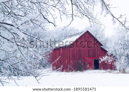 Red barn with soft focused, ice and snow covered branches in the foreground.
