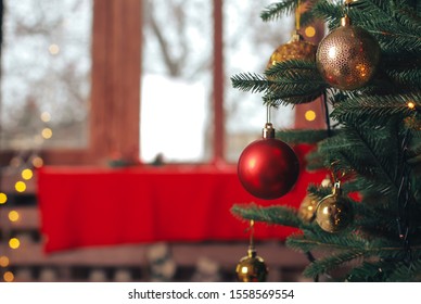 Red bauble hanging on Christmas tree. Blurry home interior background. Ball, light bokeh, New Year, celebration, holiday, copy space