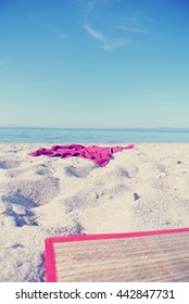 Red Beach Towel And Straw Mat Left On White Sandy Beach, On A Sunny Summer Day. Image Filtered In Faded, Retro, Instagram Style With Soft Focus; Nostalgic Concept Of Summer Travel. No People.