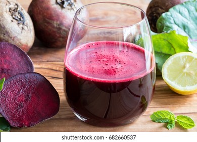 Red beet juice in a glass on a wooden background with lemon and beet greens