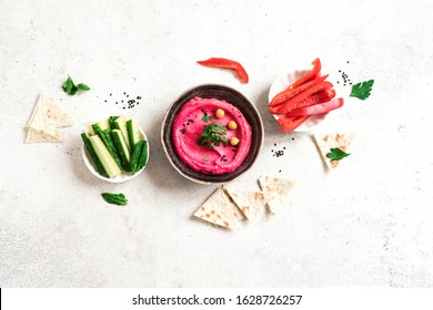 Red Beetroot Hummus bowl, healthy vegan dip. Traditional Middle eastern beet hummus,  spread  with pita bread and vegetables. Top view, copy space.