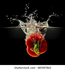 Red bell pepper falling in water with splash on black background.