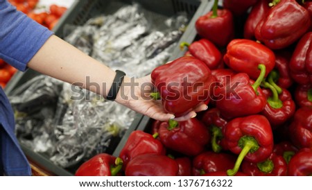 Red Bell pepper on supermarket shelf . Woman's hand choosing red pepper in store . concept of choise .
