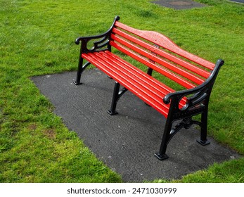 A red bench sits on a concrete slab in a grassy area. The bench is empty and the grass is lush and green. Classic metal cast old style design. Nobody. - Powered by Shutterstock