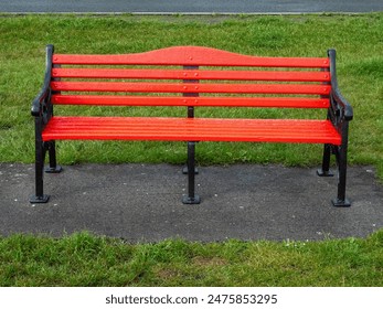 A red bench sits on a concrete slab in a grassy area. The bench is empty and the grass is lush and green. Classic metal cast old style design. Nobody. - Powered by Shutterstock