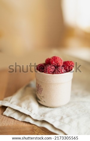 Red berries in a cup in a roustic style. Close up of fresh ruspberries in a cup on a wooden table.