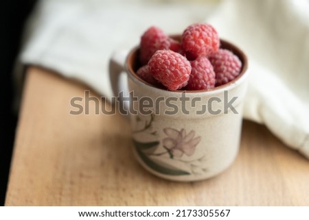 Red berries in a cup in a roustic style. Close up of fresh ruspberries in a cup on a wooden table.