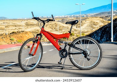 A red bicycle is parked on a road in front of a mountain. The bike is a mountain bike, and it is ready for a ride - Powered by Shutterstock
