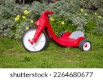 A child’s red big wheel toy on the grass