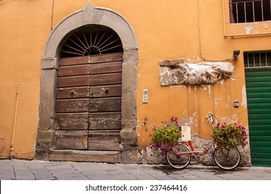 Red bike loaded with flowers standing in front of an old wooden door in a traditional Italian medieval city center. Tuscany, Italy. - Powered by Shutterstock