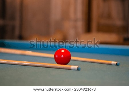 Red billiard ball with a cue lies on a green billiard table, close-up. Billiards pool table retro vintage style