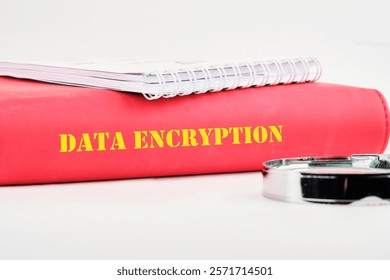 A red binder labeled data encryption rests on a surface alongside a silver binder clip and a notepad, illustrating the importance of secure information management practices.