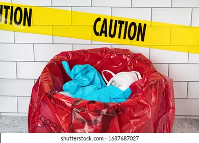 Red Biohazard Trash Bag With Used N95 Respirator Mask, Medical Exam Gloves And Caution Tape. Concept Of Medical Equipment Shortage During Covid-19 Coronavirus Pandemic