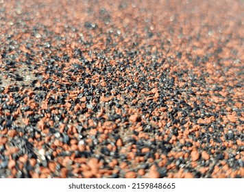 Red and black granular surface of mineral plaster with on sun (macro, angle, texture).
