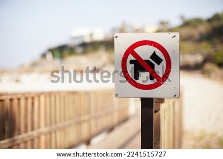 Red and black no dogs allowed sign on wooden path leading to beach