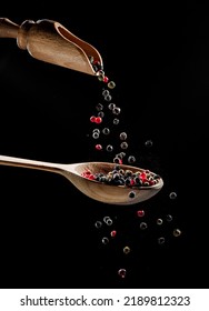 Red and black peppercorns falling down into the wooden spoon at black background.  - Shutterstock ID 2189812323