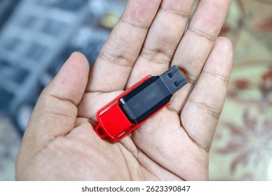 A red and black USB flash drive (Flashdisk) in hand, used to store and transfer digital files such as documents, photos, and videos.