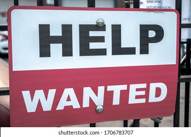 A Red Black And White Sign With Help Wanted Text Hanging On A Black Cast Iron Fence Along The Sidewalk With Two Bolts In Chicago During The COVID-19 Outbreak And Pandemic.