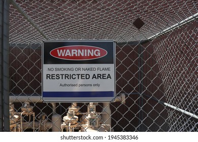 Red, black and white Warning, No Smoking or Naked Flame, Restricted Area, Authorised Persons Only sign on a fence at an industrial workplace site