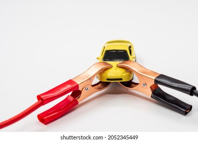Red and black wire automotive clips or battery clamps on a yellow toy car on a white background. The concept of a quick start of the battery, starting the automobile engine in winter.