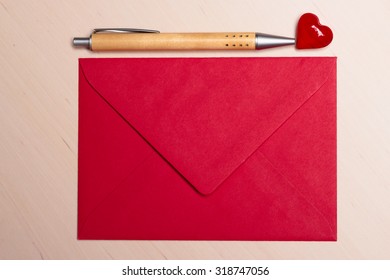 Red blank envelope little heart and pen on wooden surface. Valentine day card, love or wedding greeting concept.