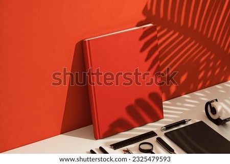 Red blank hardcover book mockup, template on red and white background with palm leaf shadow. Stationary flat lay, knolling